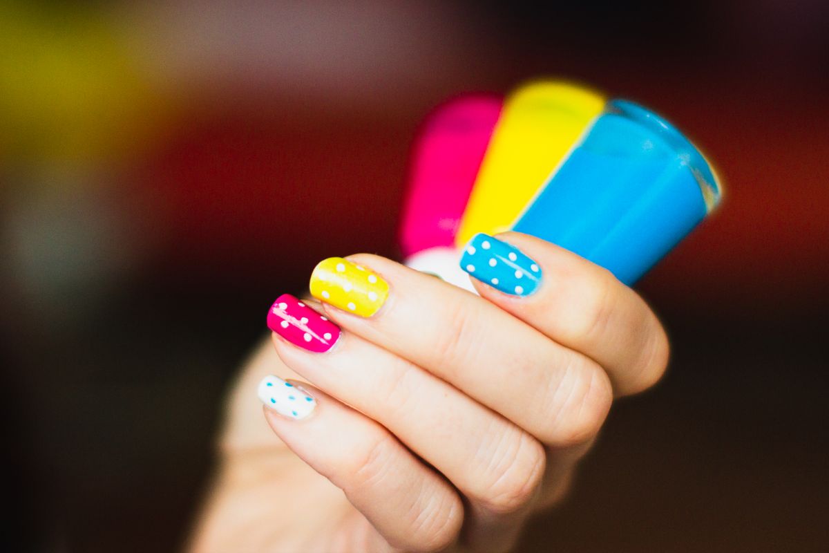 Mano con nail art de lunares de colores junto a varios esmaltes